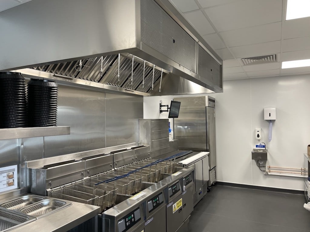 Commercial kitchen with white PVC hygienic wall panels, stainless steel cooking equipment, and ventilation hood for food-safe cleanroom cladding