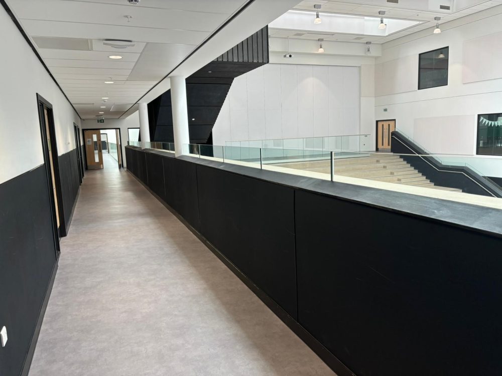 School corridor with dark PVC hygienic wall panels installed as wainscoting alongside white upper wall cladding for durable, easy-to-clean surfaces
